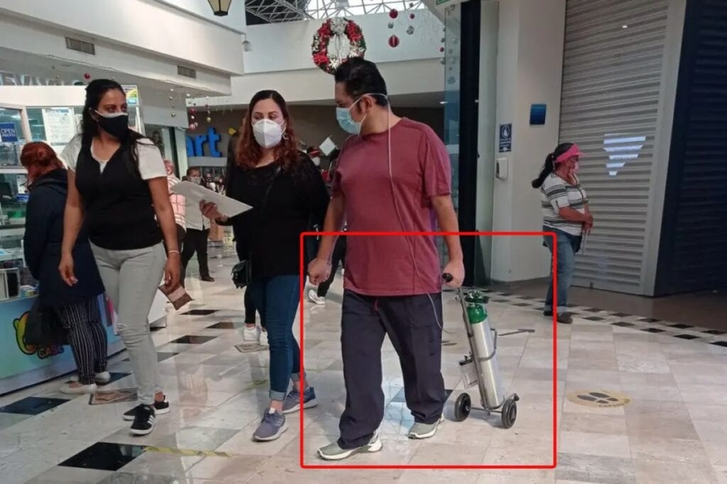 Una usuaria de redes sociales subió una imagen de dos mujeres y un hombre caminando por un centro comercial, mientras que él jala su tanque de oxígeno en medio de la pandemia de covid-19.